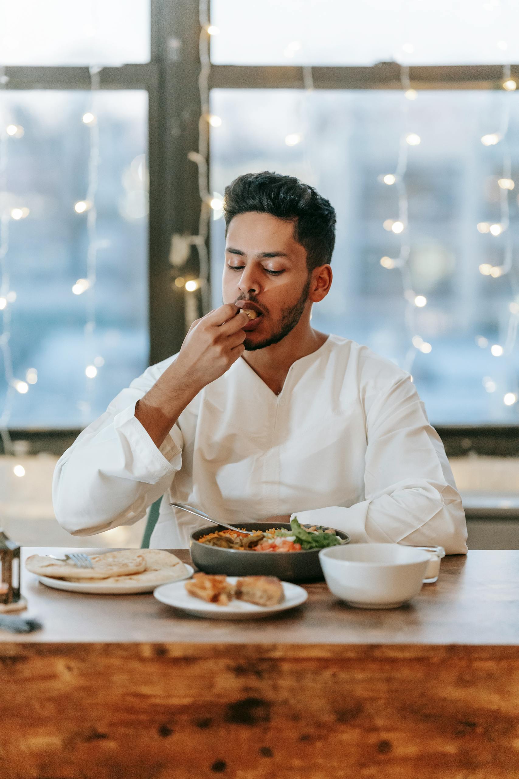 A Muslim man in a thobe enjoys a traditional iftar meal indoors, showcasing cultural dining customs.