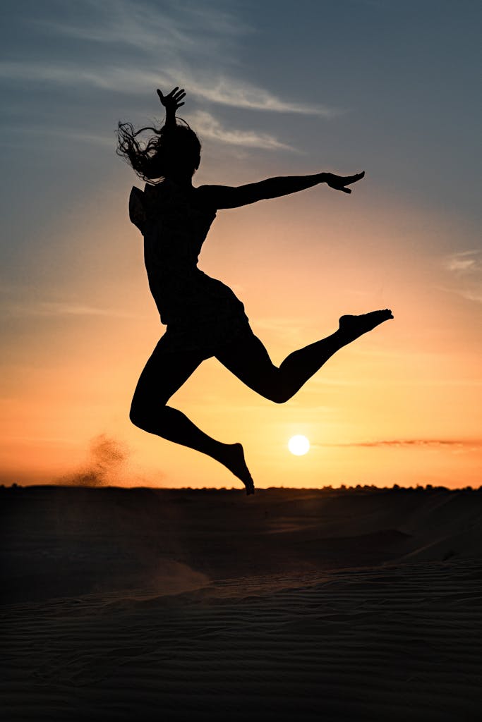 A silhouette of a woman gracefully leaping against a sunset backdrop on a beach.