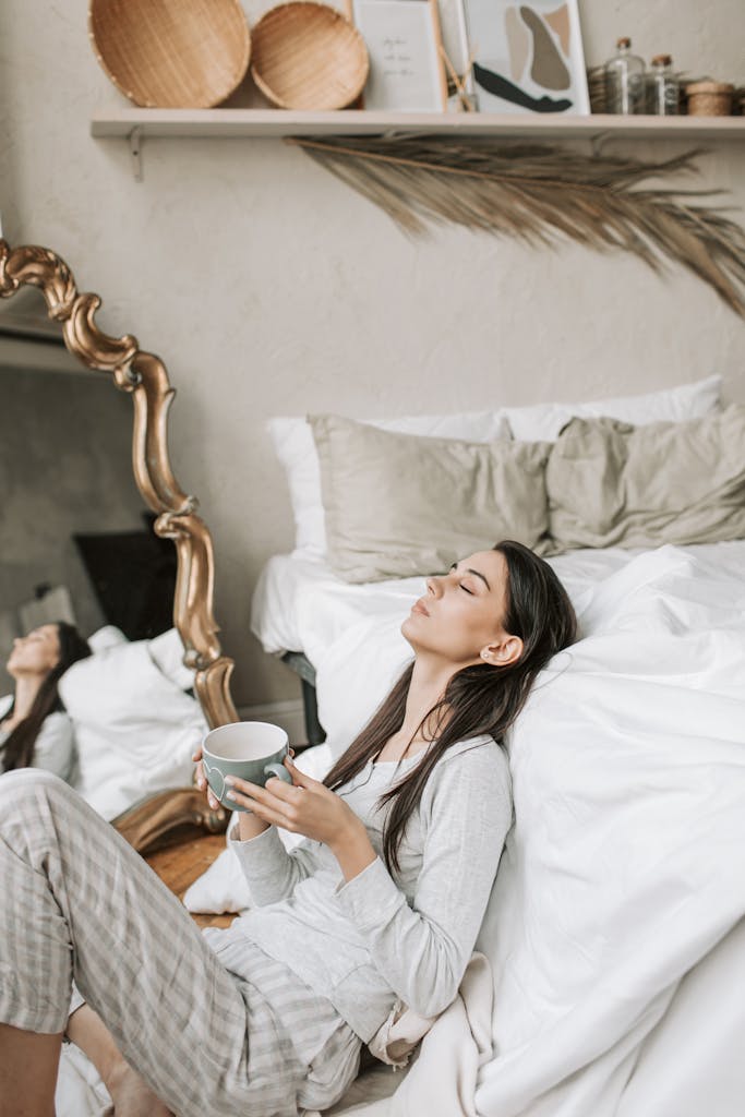 Woman enjoying a peaceful morning with coffee, sitting in a cozy bedroom with modern decor.